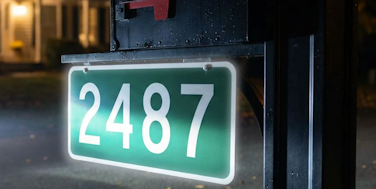 Green and white reflective address sign hanging from a black mailbox